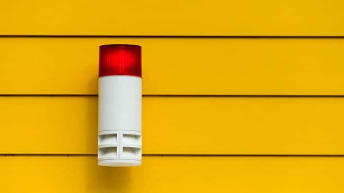 Eine rote Alarmlampe montiert an einer gelben Wand mit Lattenstruktur.