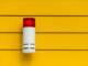 Eine rote Alarmlampe montiert an einer gelben Wand mit Lattenstruktur.