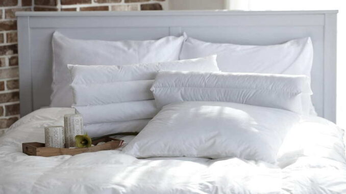 Ein gemütliches Bett mit weißen Kissen, Büchern und einer Brille, die auf der Bettdecke liegen.
