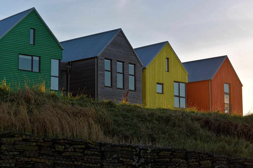 Farbenfrohe Häuser mit Satteldächern stehen auf einem Hügel, hinter denen sich der Himmel abzeichnet.