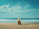 Ein einzelner Liegestuhl unter einem Sonnenschirm steht am leeren Strand mit Blick auf das Meer und den klaren blauen Himmel.