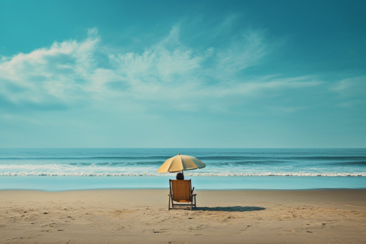 Ein einzelner Liegestuhl unter einem Sonnenschirm steht am leeren Strand mit Blick auf das Meer und den klaren blauen Himmel.