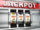 Ein Spielautomat zeigt das Wort 'JACKPOT' über drei Walzen mit Symbolen, darunter die Nummer sieben und Früchte.