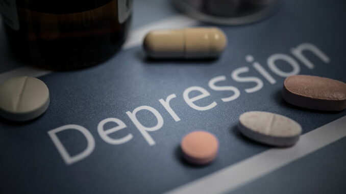 Auf dem Bild sind verschiedene Medikamententabletten neben einem Fläschchen auf einem Untergrund mit der Aufschrift 'Depression' zu sehen.