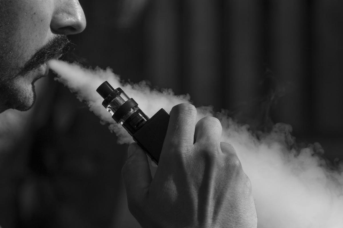 Ein Mann benutzt ein E-Zigaretten-Gerät, aus dem Rauch austritt.