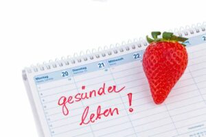 Ein Kalender mit einer Erdbeere und dem handschriftlichen Text 'gesunder leben!' auf einer Seite, die mit Montag beginnt.