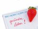 Ein Kalender mit einer Erdbeere und dem handschriftlichen Text 'gesunder leben!' auf einer Seite, die mit Montag beginnt.