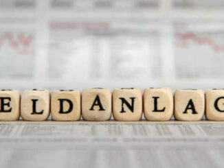 Würfel mit Buchstaben formen das Wort 'Geldanlage' vor unscharfen Zeitungshintergrund.