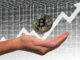Eine Hand hält eine Bitcoin-Münze, mit einem steigenden Pfeildiagramm im Hintergrund, symbolisch für den Anstieg des Kryptowährungswertes.