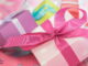 Auf dem Bild sind bunt verpackte Geschenke mit Schleifen auf einem rosafarbenen Hintergrund zu sehen.