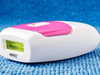 Ein tragbares, weiß-pinkes Epiliergerät liegt auf einer blauen Textiloberfläche.