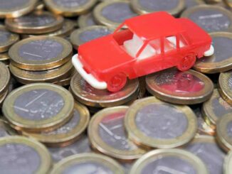Ein rotes Spielzeugauto steht auf vielen übereinandergestapelten Ein-Euro-Münzen.