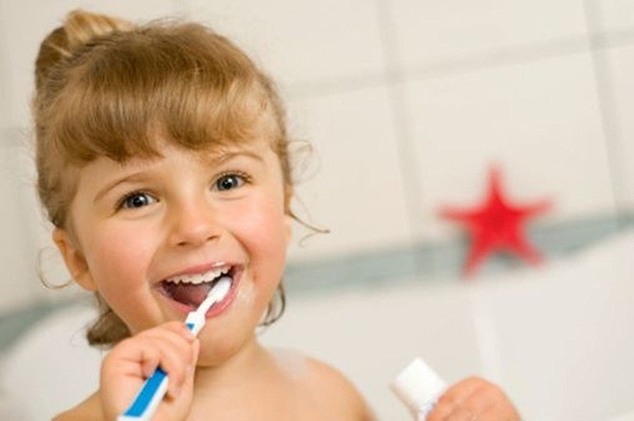 Ein kleines Mädchen putzt sich lächelnd die Zähne im Badezimmer.