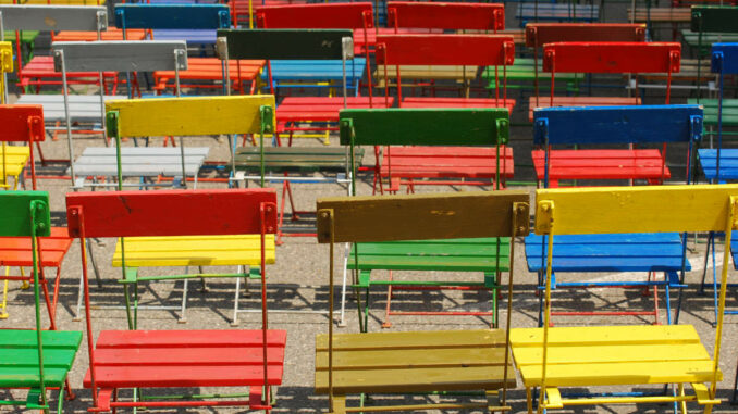 Bunte Stühle in Rot, Grün, Gelb und Blau sind ordentlich im Freien aufgestellt.