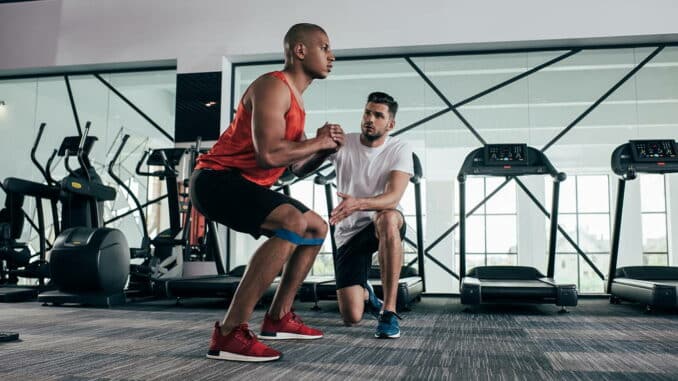 Ein Mann springt während einer Trainingsübung in einem Fitnessstudio, während ein anderer ihm zuschaut und Anweisungen gibt.