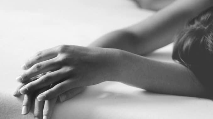 Eine Person liegt entspannt auf dem Bauch, wobei nur ihre Hand und der Arm auf einer weißen Oberfläche im Fokus sind.