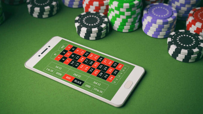 Ein Smartphone mit einer Roulette-App auf einem grünen Tisch umgeben von bunten Casino-Chips.