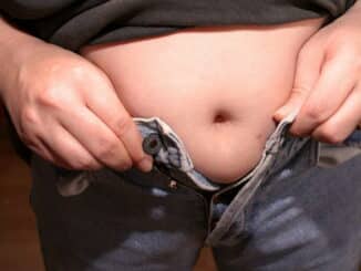 Eine Person hebt ihr Shirt hoch, um ihre unzureichende Passform einer Jeans zu zeigen.