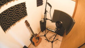 Ein kleines Heimstudio mit Gitarre, Mikrofonständer und Schalldämmplatten an den Wänden.