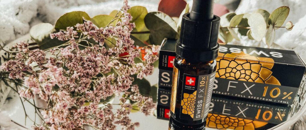 Auf dem Bild ist eine Flasche CBD-Öl neben einer Verpackung, umgeben von trockenen Blumen auf einem weißen Tablett.