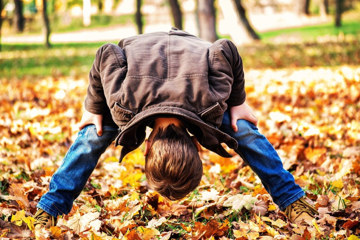 Ein Kind macht einen Kopfstand auf einem Blätterhaufen im Herbstpark.