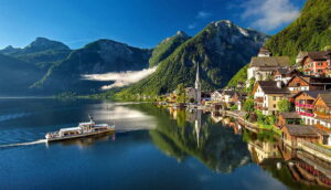 Bunte Häuser an einem ruhigen See mit Bergen im Hintergrund und einem Boot auf dem Wasser.